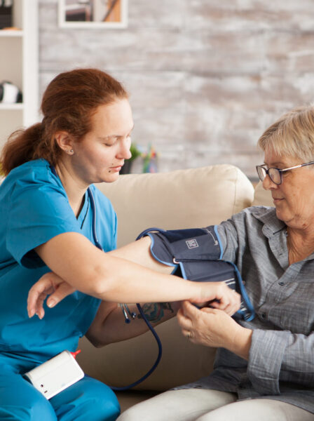 Female nurse using digital blood pressure device on senior woman in nursing home.